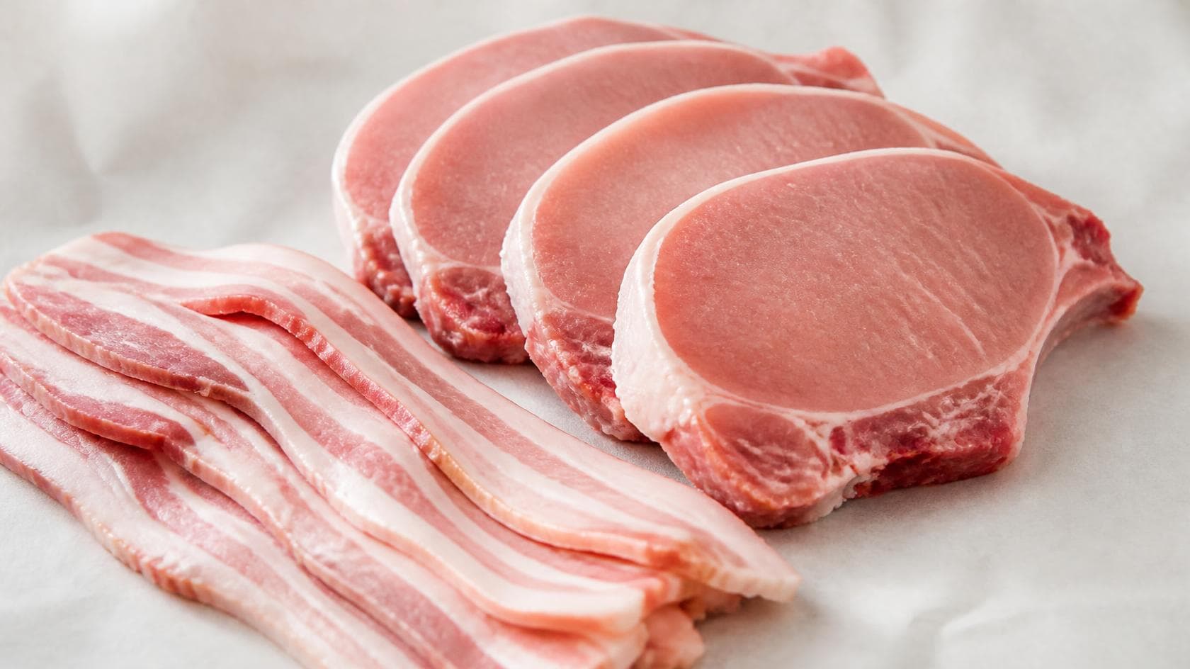 Raw pork chops and bacon at a grocery store meat counter, illustrating the pork price-fixing settlement
